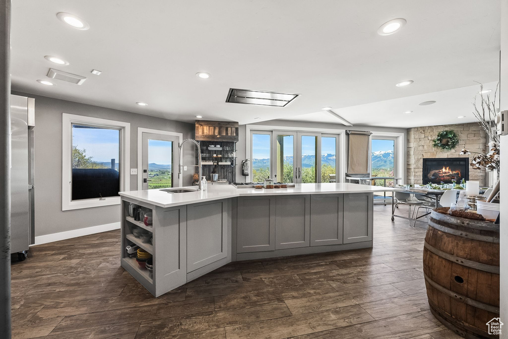 Kitchen featuring a stone fireplace, a center island with sink, sink, and gray cabinetry