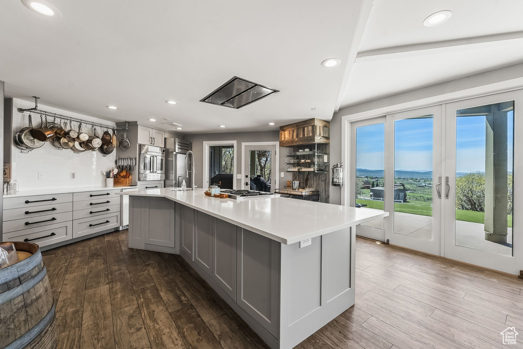 Kitchen with gray cabinets, decorative backsplash, dark hardwood / wood-style floors, and a large island with sink