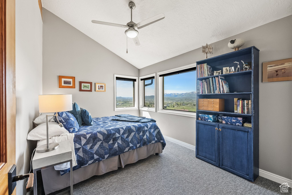 Carpeted bedroom with a textured ceiling, vaulted ceiling, and ceiling fan