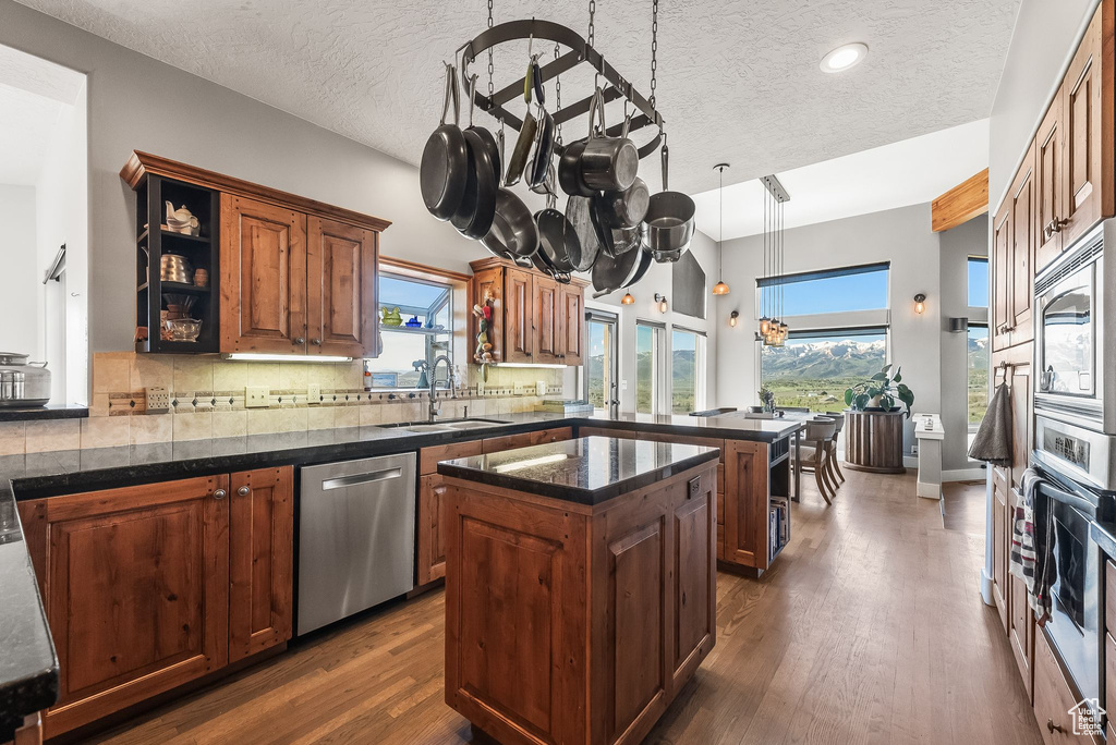 Kitchen featuring a textured ceiling, dark hardwood / wood-style floors, hanging light fixtures, a kitchen island, and appliances with stainless steel finishes