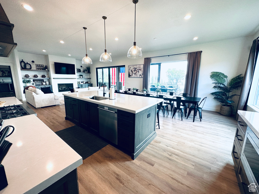 Kitchen featuring light hardwood / wood-style floors, dishwasher, pendant lighting, a center island with sink, and sink