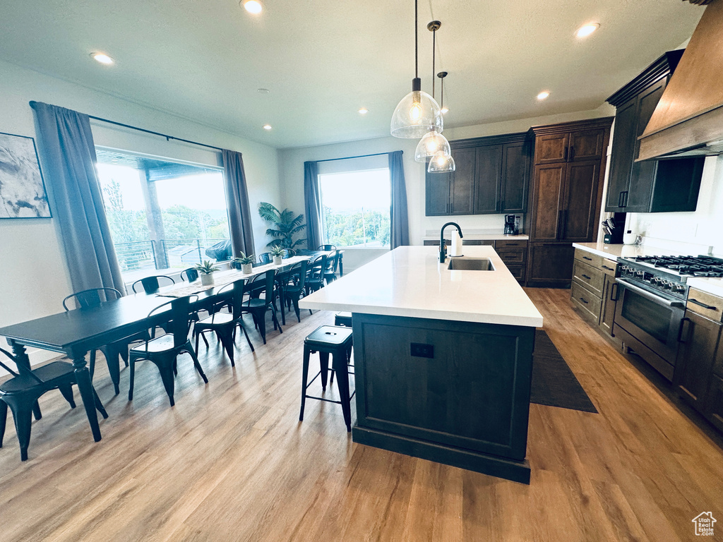 Kitchen featuring hanging light fixtures, sink, high end range, a center island with sink, and light wood-type flooring