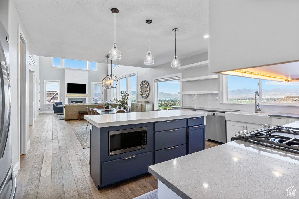 Kitchen with white cabinetry, blue cabinetry, appliances with stainless steel finishes, a center island, and light hardwood / wood-style floors