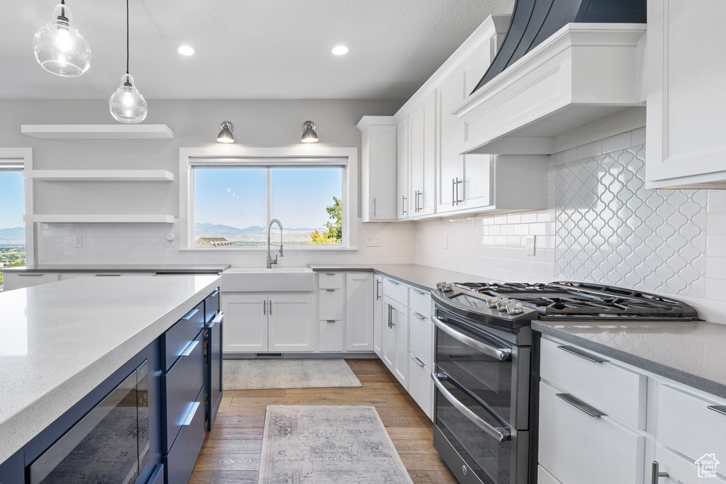 Kitchen featuring white cabinets, decorative light fixtures, stainless steel gas range oven, custom range hood, and hardwood / wood-style floors