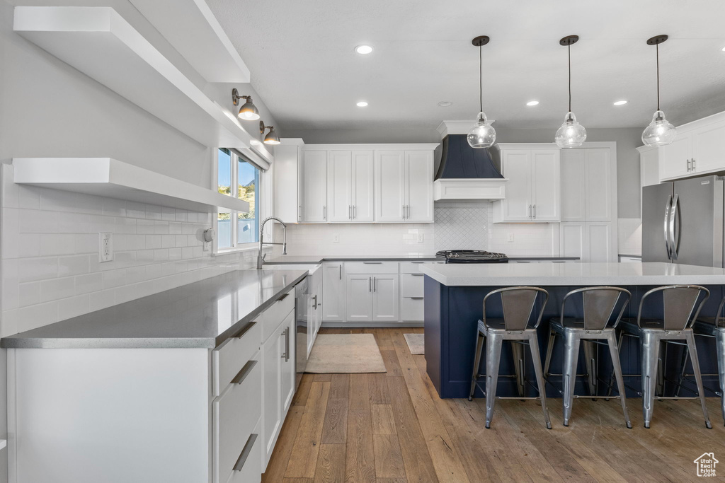 Kitchen featuring light wood-type flooring, sink, white cabinets, a kitchen island, and custom exhaust hood