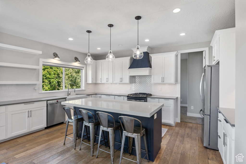 Kitchen featuring a kitchen island, white cabinetry, hardwood / wood-style flooring, stainless steel appliances, and custom range hood