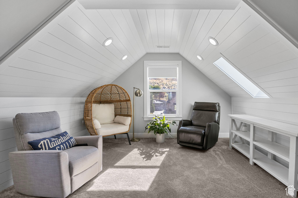 Living area with carpet flooring, wooden walls, and lofted ceiling with skylight