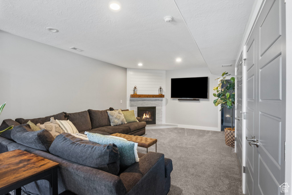 Living room featuring a textured ceiling, a fireplace, and carpet flooring