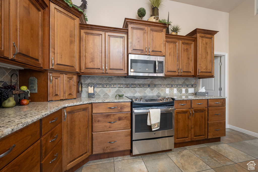 Kitchen featuring appliances with stainless steel finishes, light stone countertops, and tasteful backsplash