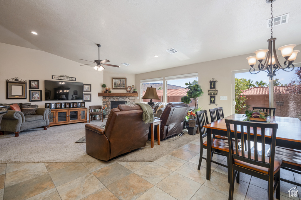 Living room with ceiling fan with notable chandelier, a stone fireplace, and lofted ceiling