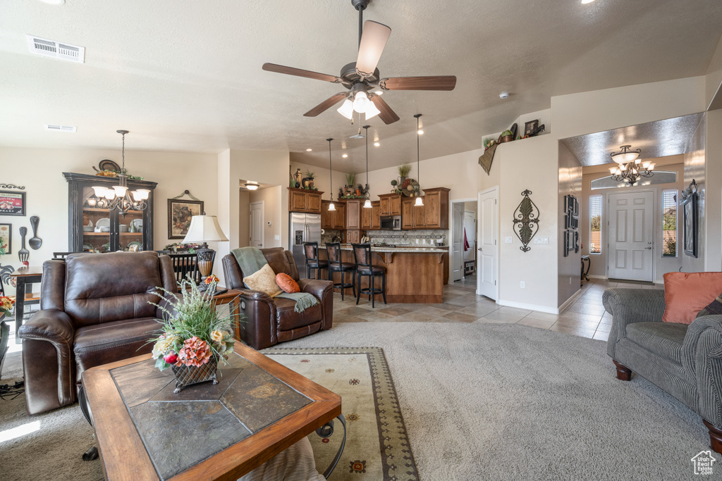 Living room featuring light tile patterned floors, ceiling fan with notable chandelier, and vaulted ceiling