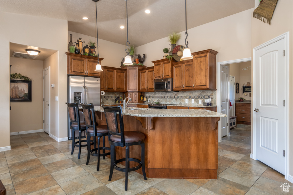 Kitchen featuring tasteful backsplash, a kitchen island with sink, light stone countertops, and decorative light fixtures