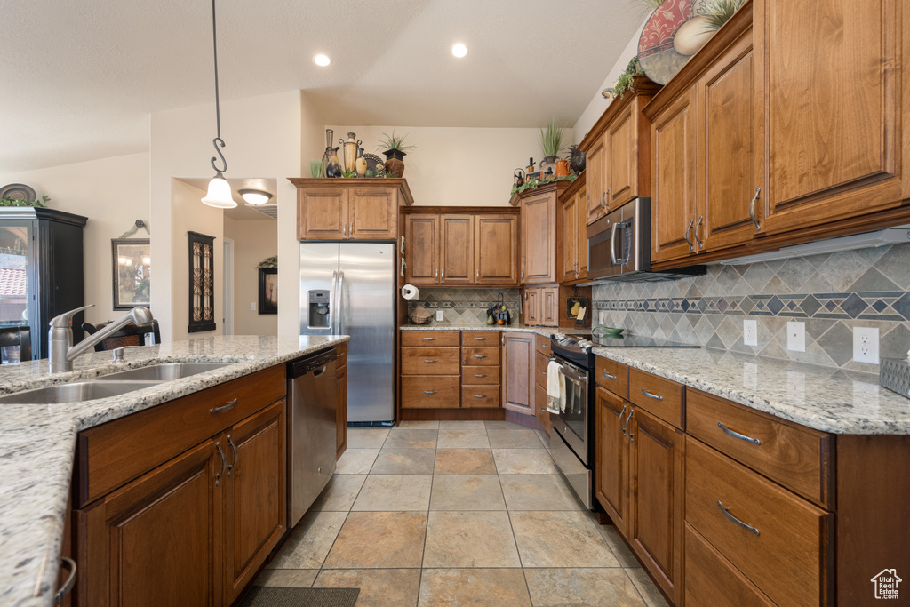 Kitchen with pendant lighting, sink, decorative backsplash, appliances with stainless steel finishes, and light stone countertops