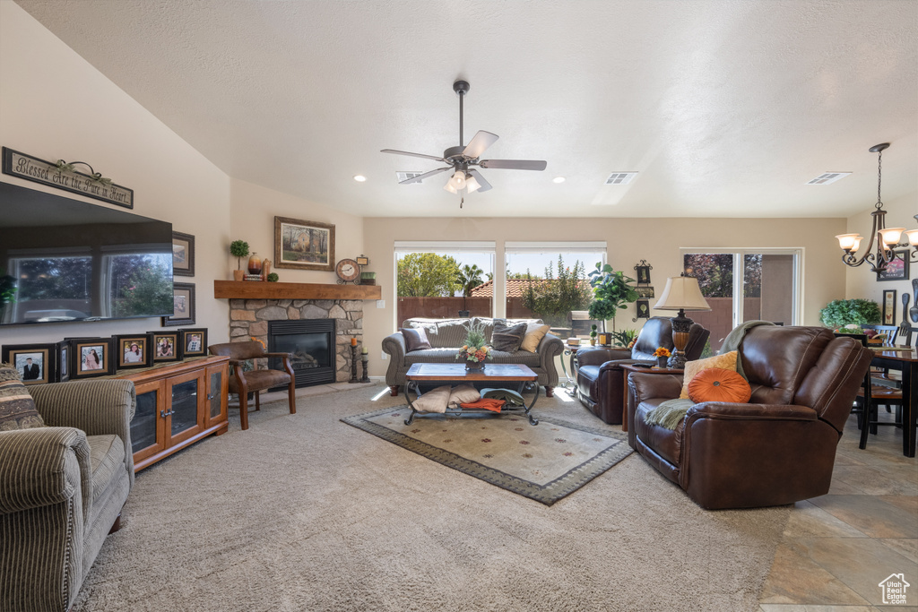 Carpeted living room with ceiling fan with notable chandelier and a stone fireplace