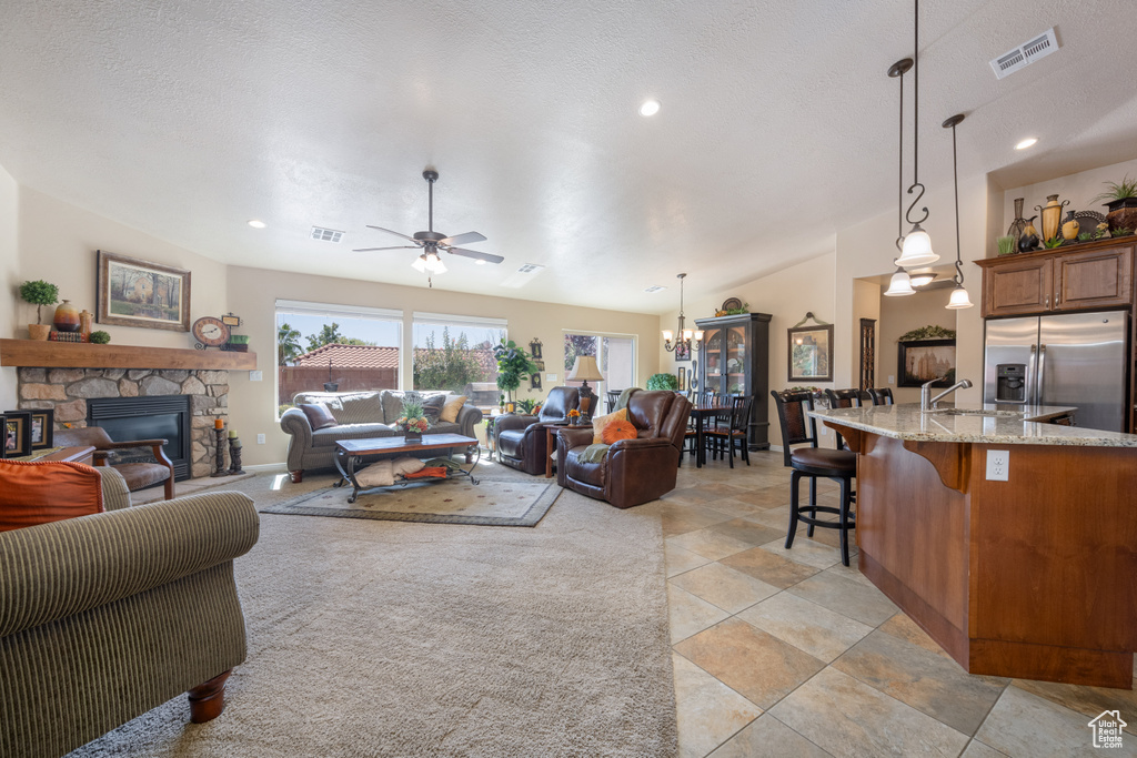 Living room with ceiling fan with notable chandelier, a textured ceiling, sink, and a stone fireplace