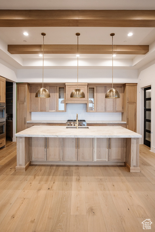 Kitchen featuring pendant lighting, beamed ceiling, light wood-type flooring, and a large island with sink