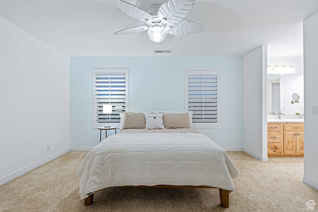 Bedroom featuring ceiling fan, light colored carpet, ensuite bath, and sink