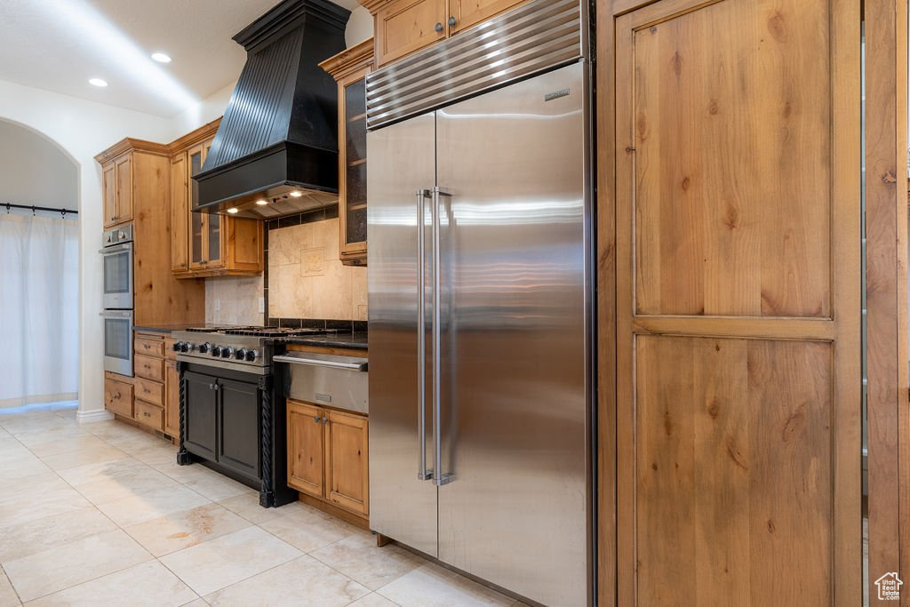 Kitchen with light tile patterned floors, appliances with stainless steel finishes, backsplash, and custom range hood