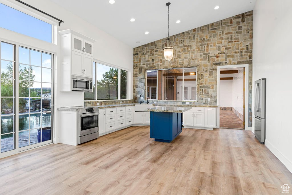 Kitchen with appliances with stainless steel finishes, white cabinetry, a kitchen island, and decorative light fixtures