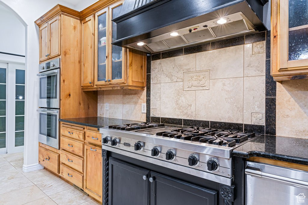 Kitchen featuring dark stone countertops, appliances with stainless steel finishes, custom range hood, and decorative backsplash