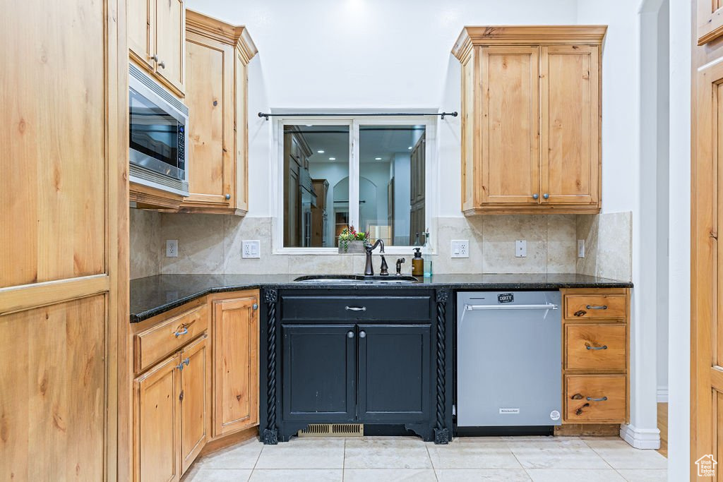 Kitchen with dark stone counters, sink, light tile patterned floors, and stainless steel appliances