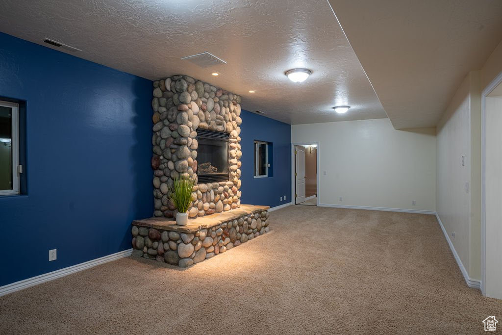 Unfurnished living room with carpet, a textured ceiling, and a stone fireplace