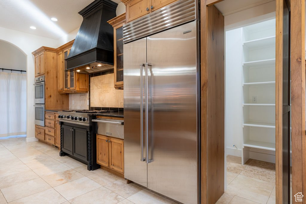 Kitchen with light tile patterned floors, appliances with stainless steel finishes, tasteful backsplash, and premium range hood