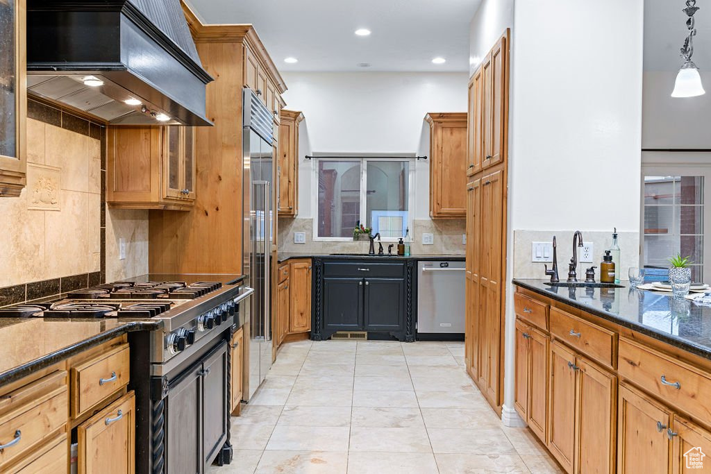 Kitchen featuring pendant lighting, sink, appliances with stainless steel finishes, custom range hood, and dark stone countertops