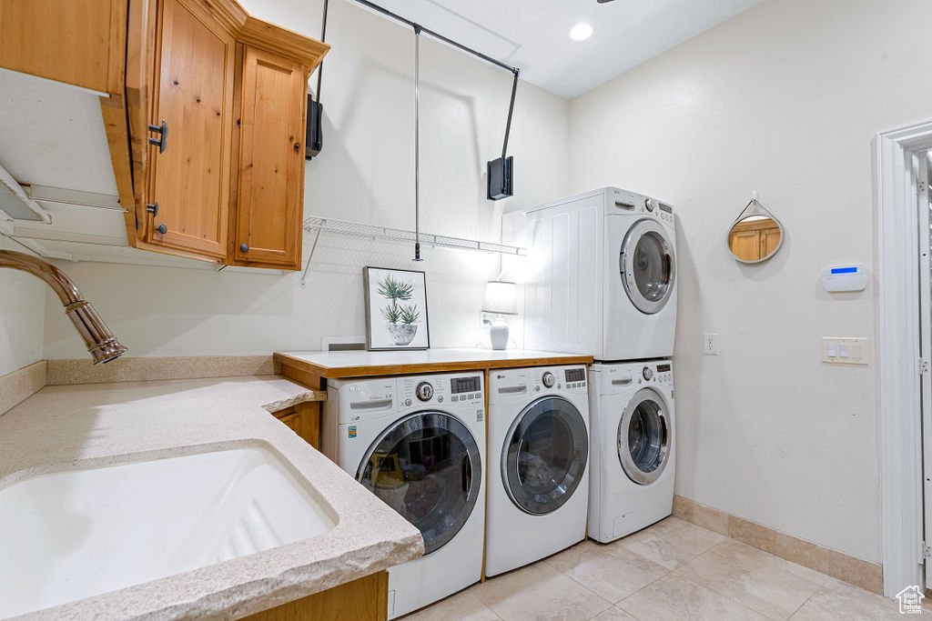 Laundry room with cabinets, stacked washer and dryer, light tile patterned flooring, sink, and washer and clothes dryer