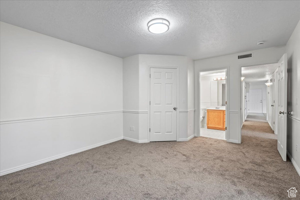 Unfurnished bedroom featuring a textured ceiling, light carpet, ensuite bathroom, and a closet