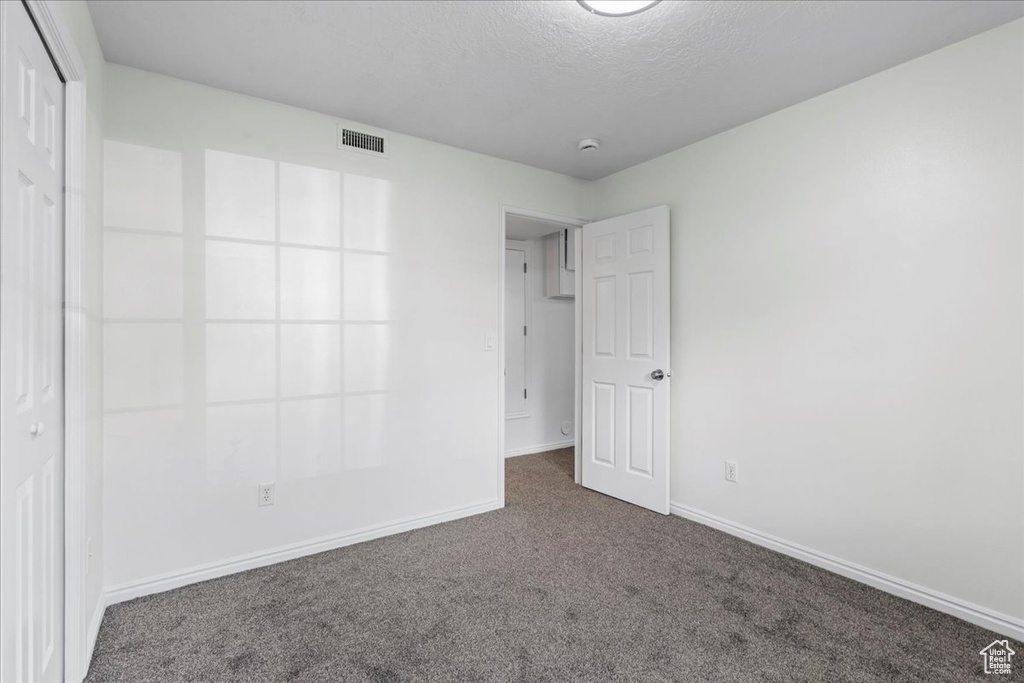 Unfurnished bedroom with a closet, dark colored carpet, and a textured ceiling