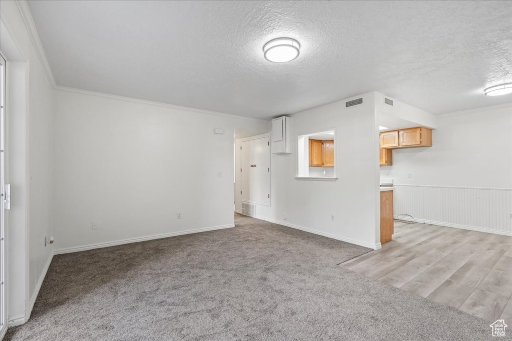 Unfurnished living room featuring light carpet, a textured ceiling, and crown molding