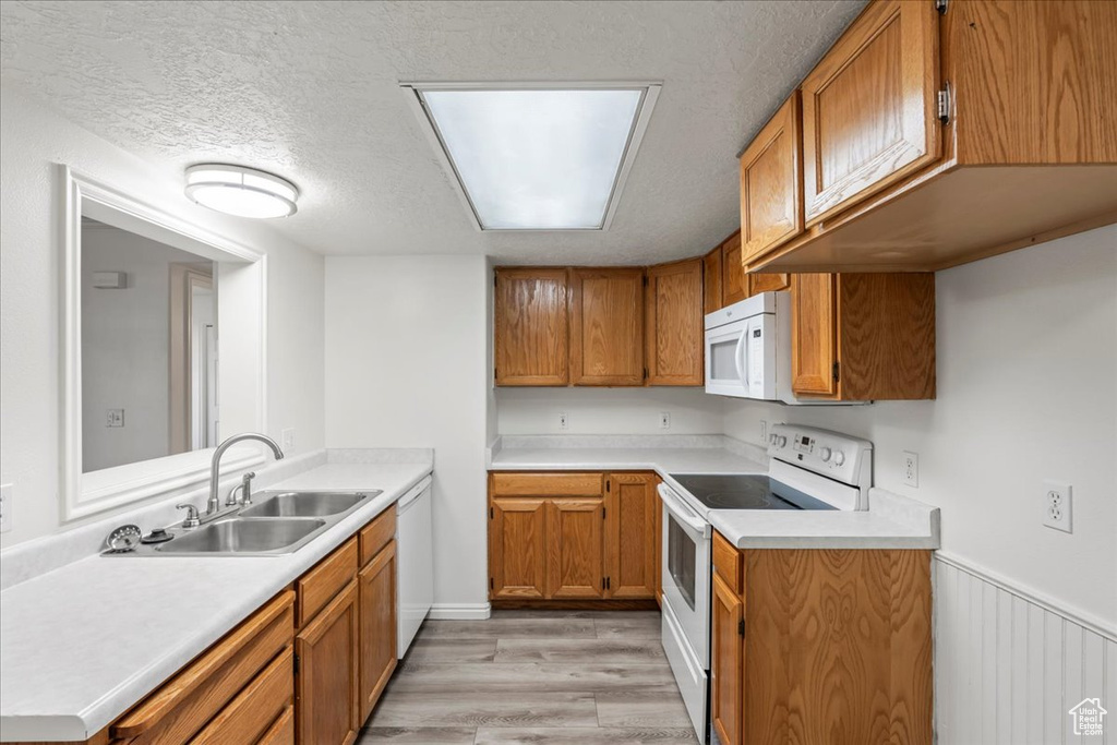 Kitchen with a textured ceiling, white appliances, light hardwood / wood-style floors, and sink