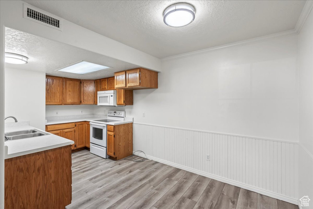 Kitchen with light wood-type flooring, white appliances, crown molding, and sink