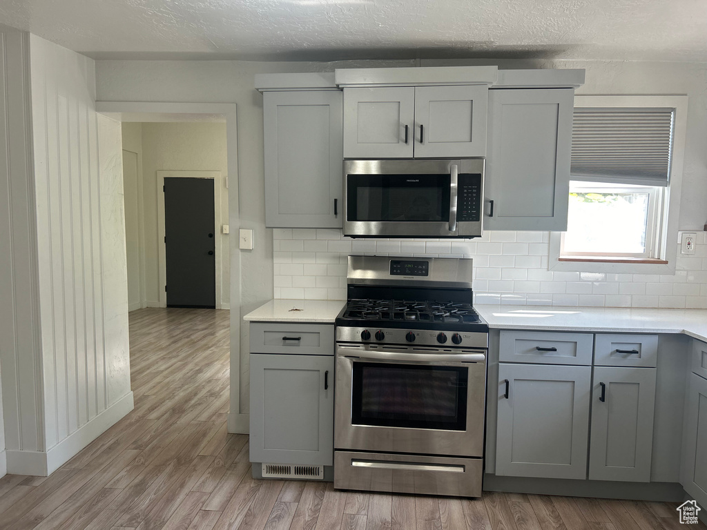 Kitchen with light hardwood / wood-style floors, a textured ceiling, gray cabinetry, stainless steel appliances, and decorative backsplash