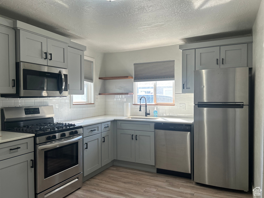 Kitchen with appliances with stainless steel finishes, light wood-type flooring, sink, and gray cabinetry