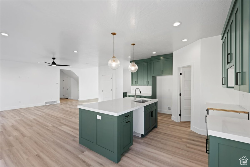 Kitchen featuring ceiling fan, decorative light fixtures, a center island with sink, sink, and green cabinets