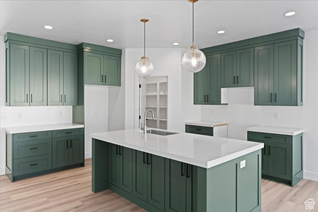 Kitchen with pendant lighting, light hardwood / wood-style flooring, a kitchen island with sink, sink, and green cabinets