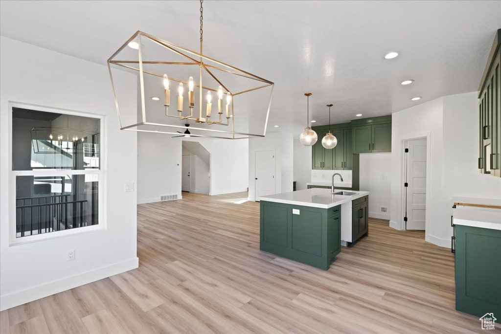 Kitchen featuring pendant lighting, green cabinetry, light hardwood / wood-style floors, and a center island with sink