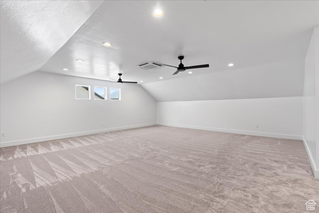 Additional living space with vaulted ceiling, ceiling fan, light colored carpet, and a textured ceiling