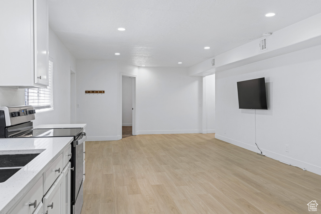 Kitchen with white cabinets, light wood-type flooring, light stone countertops, and electric range