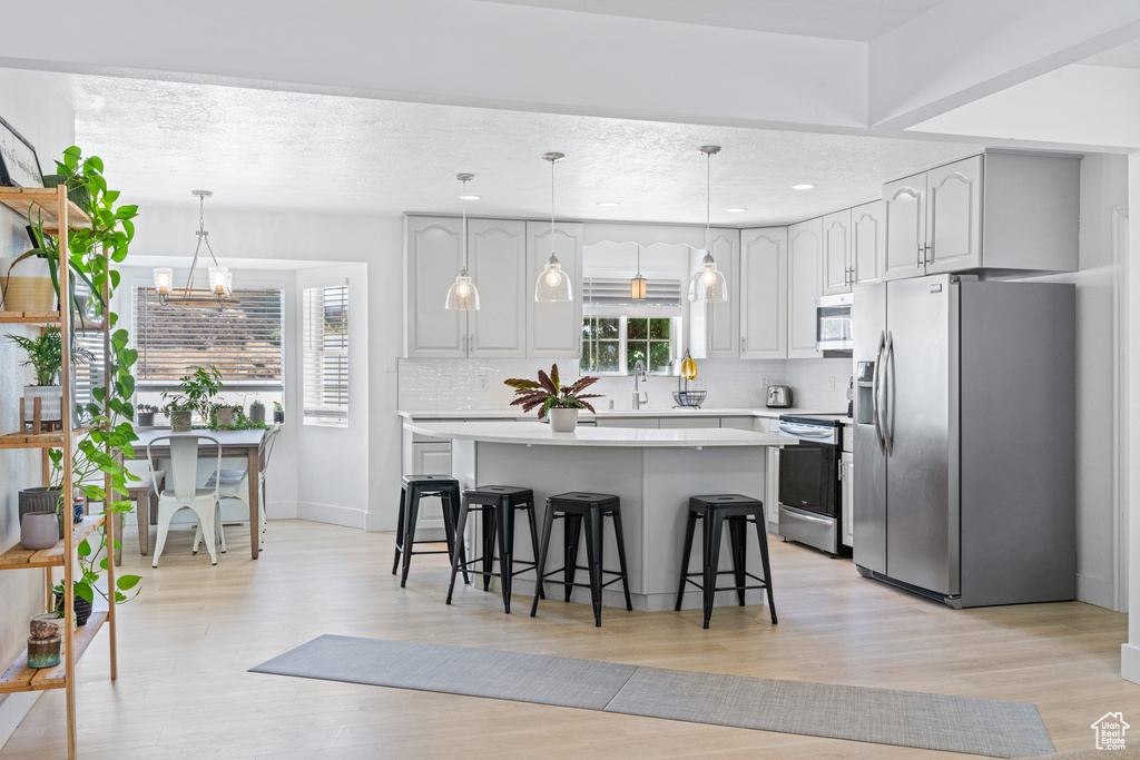 Kitchen featuring light wood-type flooring, a notable chandelier, hanging light fixtures, decorative backsplash, and appliances with stainless steel finishes