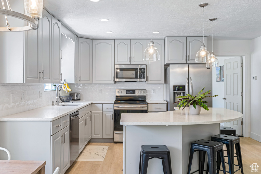 Kitchen featuring gray cabinets, stainless steel appliances, light hardwood / wood-style flooring, decorative light fixtures, and sink