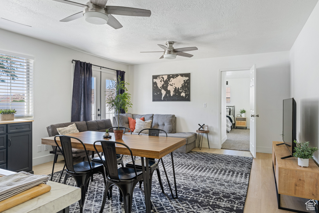 Dining area featuring light wood-type flooring, a textured ceiling, ceiling fan, and french doors