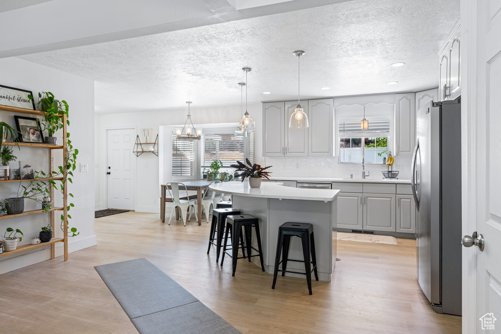 Kitchen featuring stainless steel fridge, a kitchen island, light hardwood / wood-style flooring, gray cabinets, and a notable chandelier