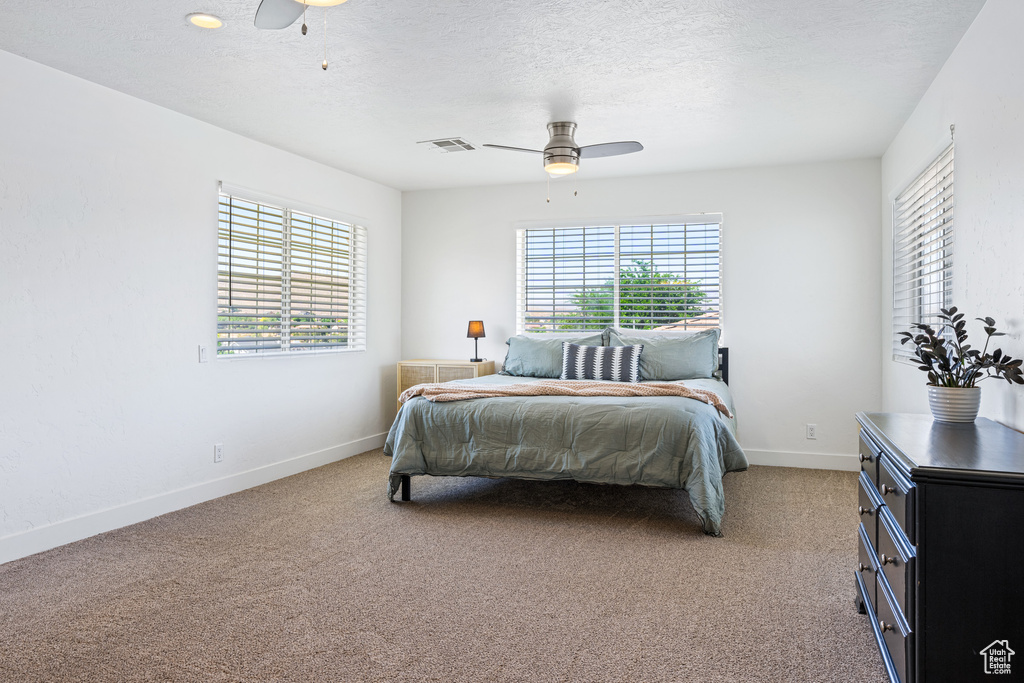 Bedroom with ceiling fan, light colored carpet, and a textured ceiling