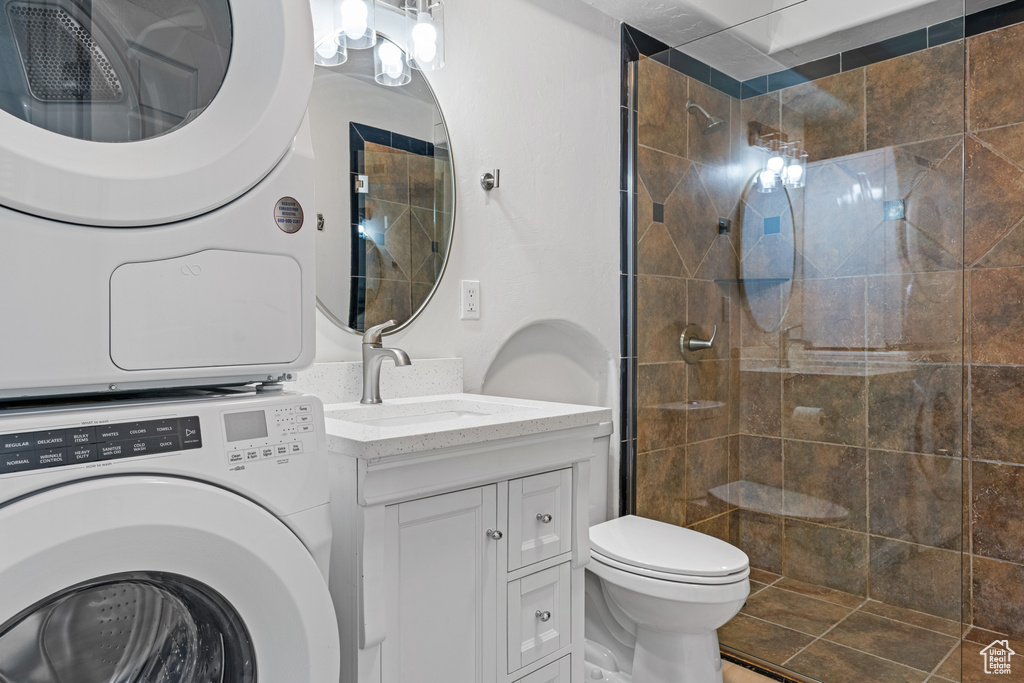 Bathroom with a tile shower, stacked washer / drying machine, vanity, and toilet