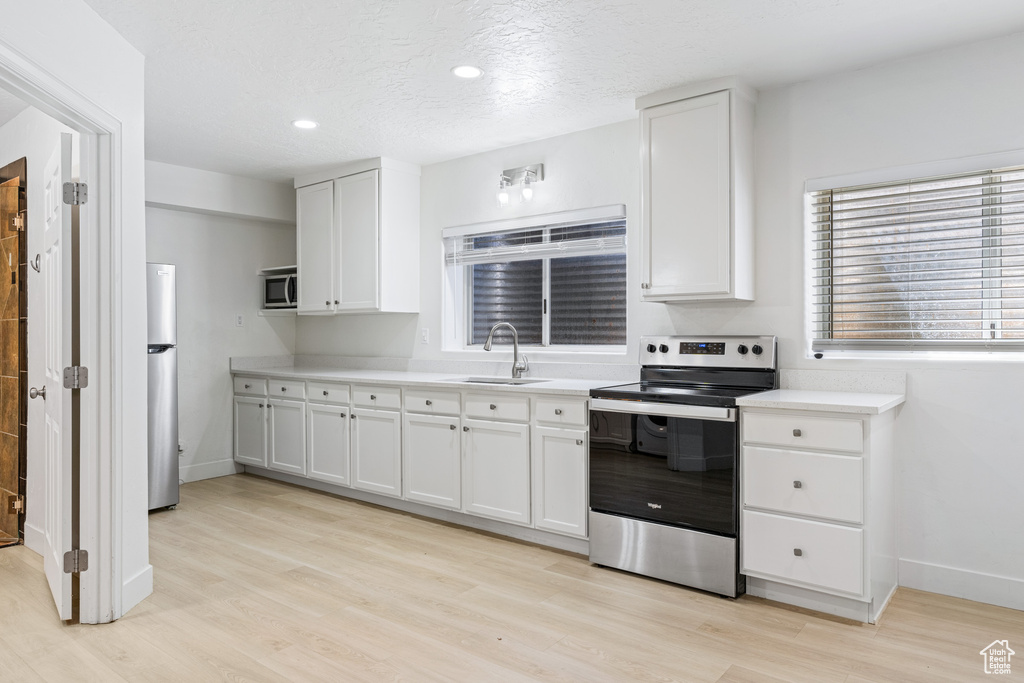 Kitchen with white cabinets, sink, a textured ceiling, stainless steel appliances, and light hardwood / wood-style floors