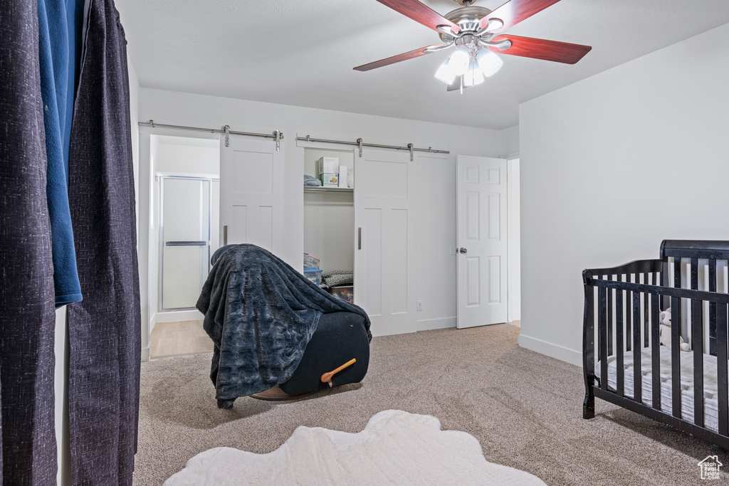 Bedroom with a barn door, a crib, light carpet, and ceiling fan