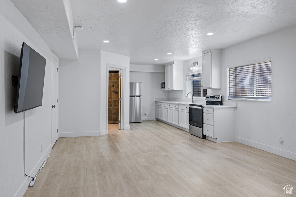 Kitchen featuring a textured ceiling, sink, white cabinetry, light hardwood / wood-style flooring, and stainless steel appliances